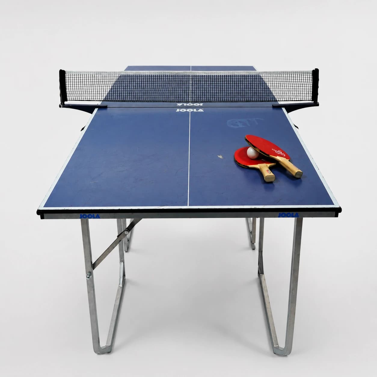 Mini Tischtennisplatte von vorn mit 2 Tischtennisschläger, die auf dem Tisch liegen mit weißem Tischtennisball